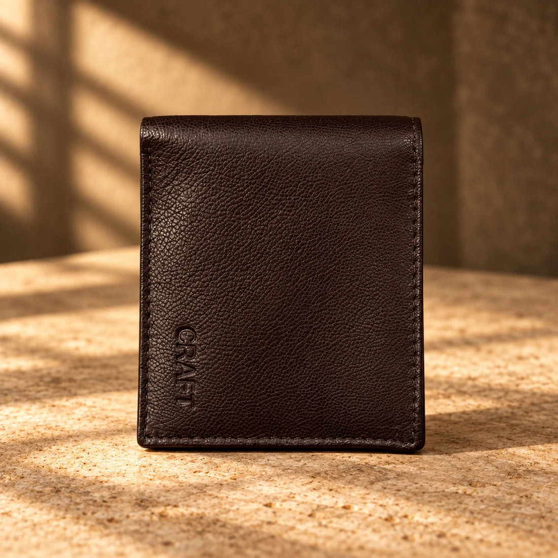 Brown CRAFT leather bifold wallet on warm stone